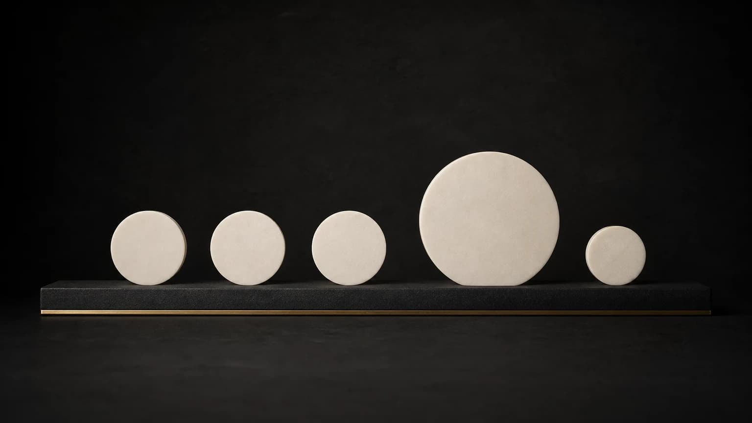 Five ivory discs rest on a short charcoal rail; the fourth is the largest, and the fifth is smaller than the third.