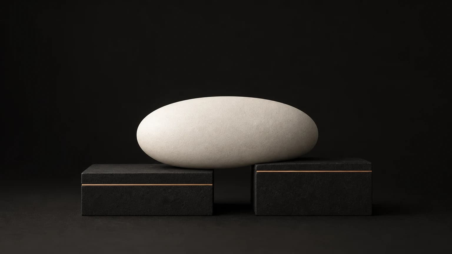 A large matte ivory stone rests across two separate charcoal plinths of different heights, each edged by its own short brass line.
