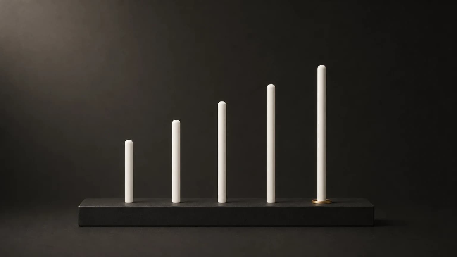 Five slim matte ivory rods of rising height stand in a row on a low charcoal plinth, with a brass ring around the base of the tallest.