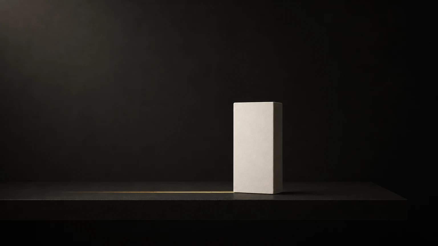 A tall matte ivory block stands near the right end of a long low charcoal table, with one thin brass line running left along the table’s edge.