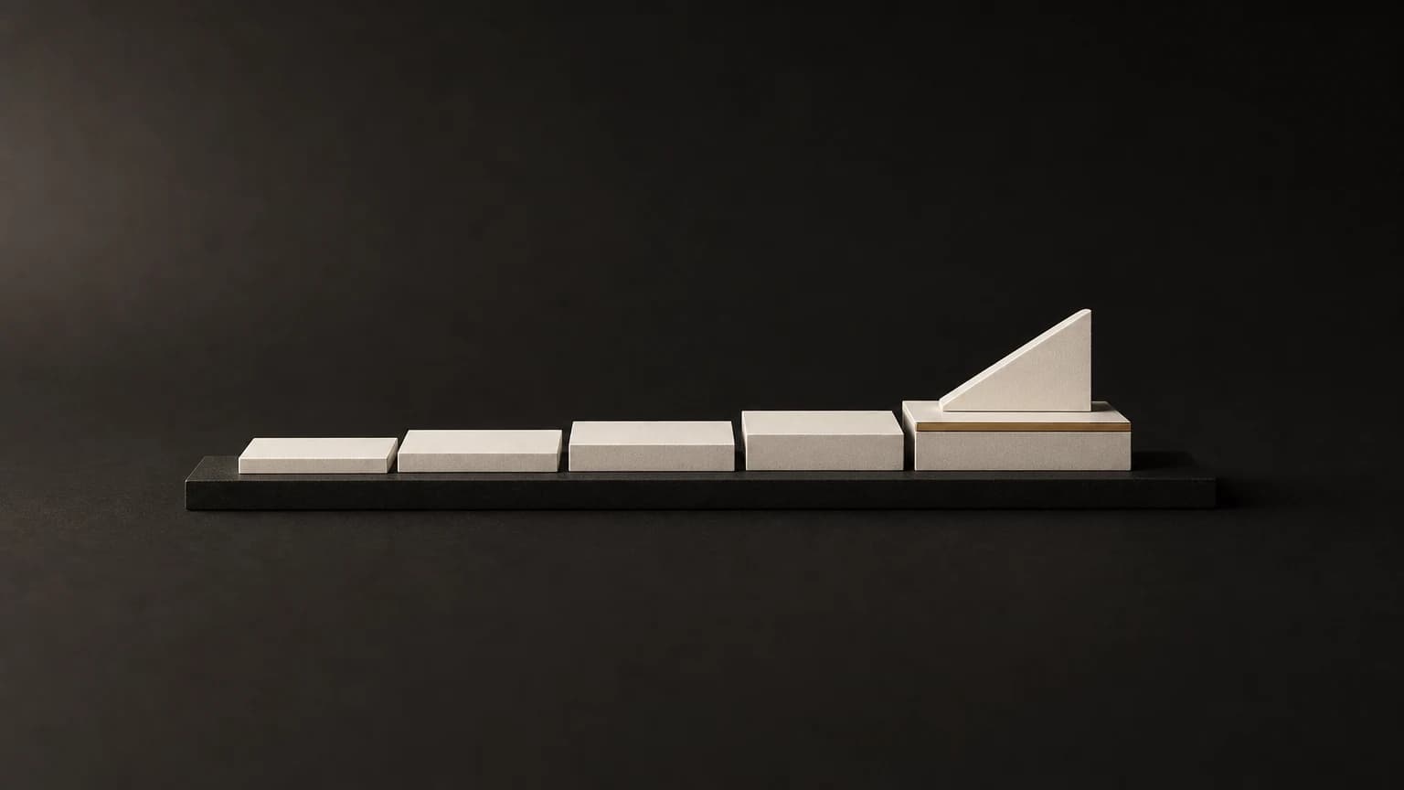 Five shallow ivory terraces rise along one low charcoal rail; a matte ivory wedge sits on the highest terrace, with a short brass line on that terrace’s leading edge.
